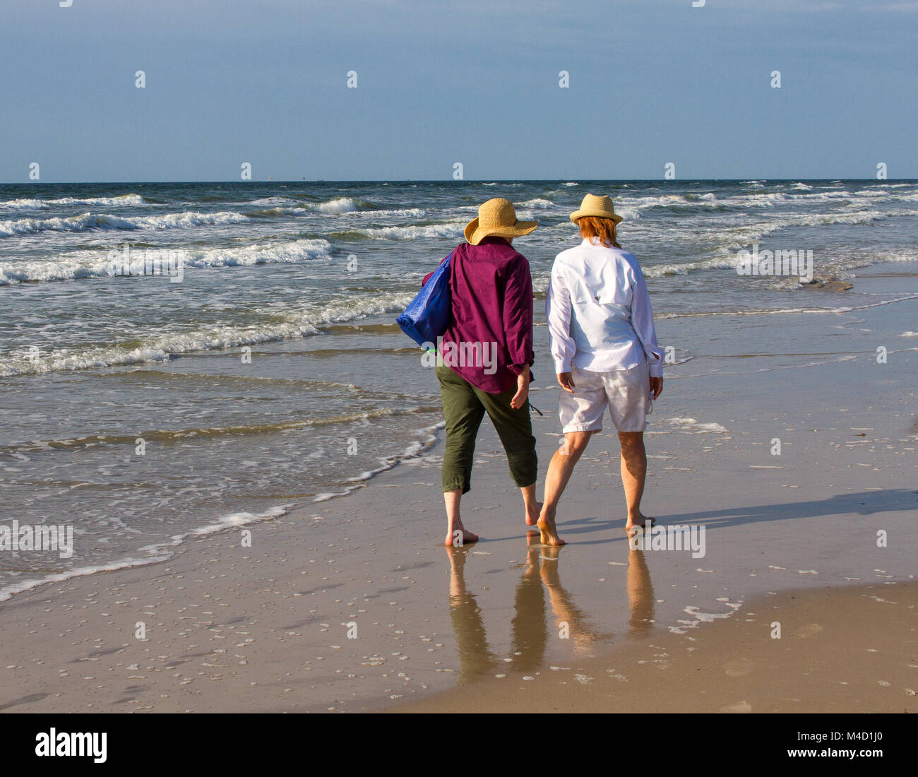 Two American senior citizen women walk together on a beach in the early morning. Stock Photo