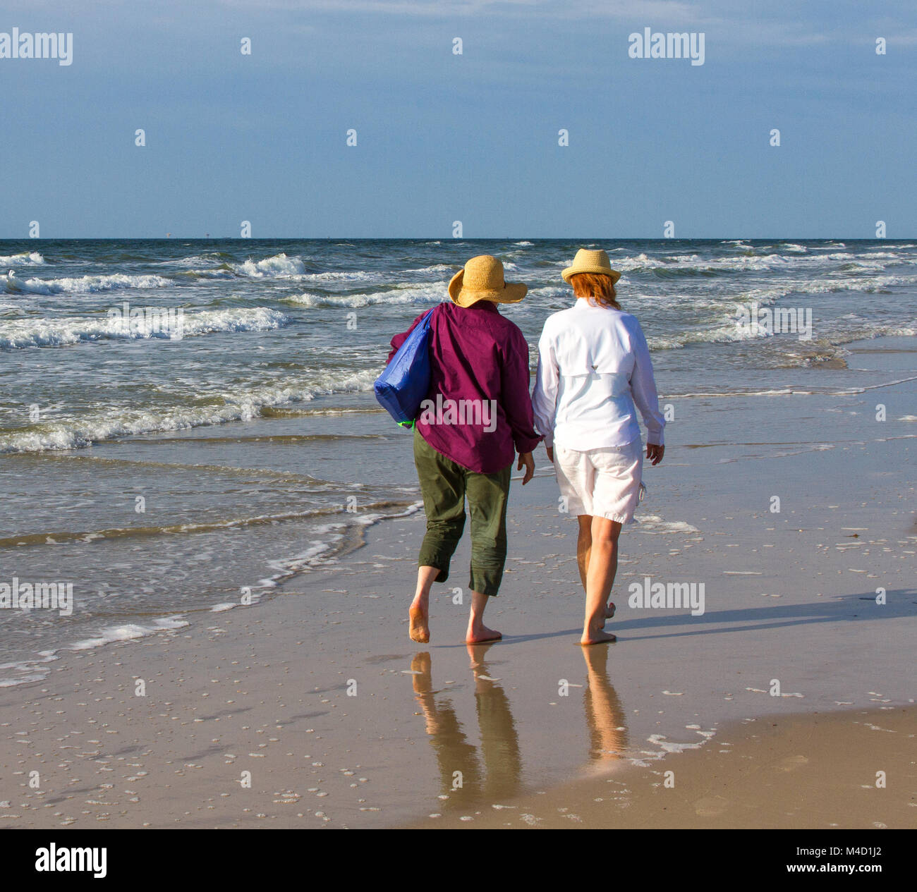 Two American senior citizen women walk together on a beach in the early morning. Stock Photo
