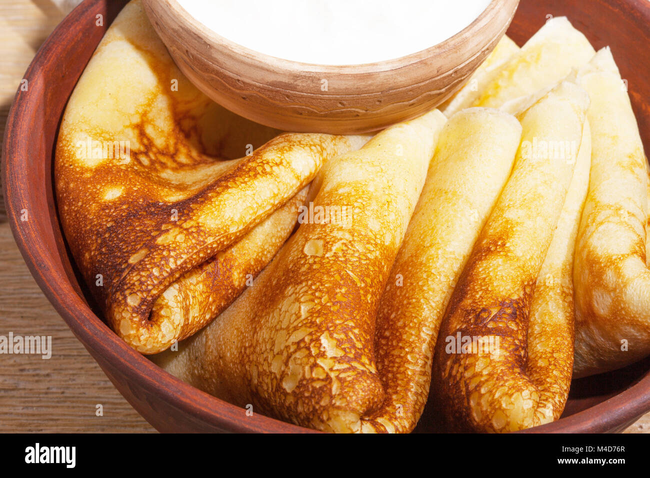 traditional oily food in vintage style: pancakes with sour cream in and a clay dish with a wooden spoon on an oak table Stock Photo