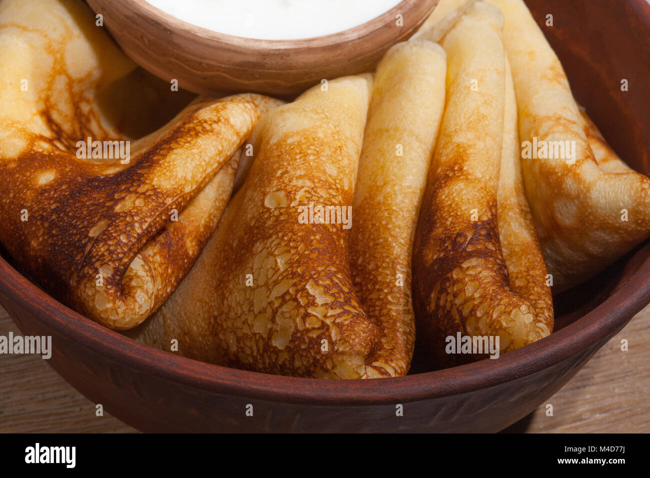 traditional oily food in vintage style: pancakes with sour cream in and a clay dish with a wooden spoon on an oak table Stock Photo