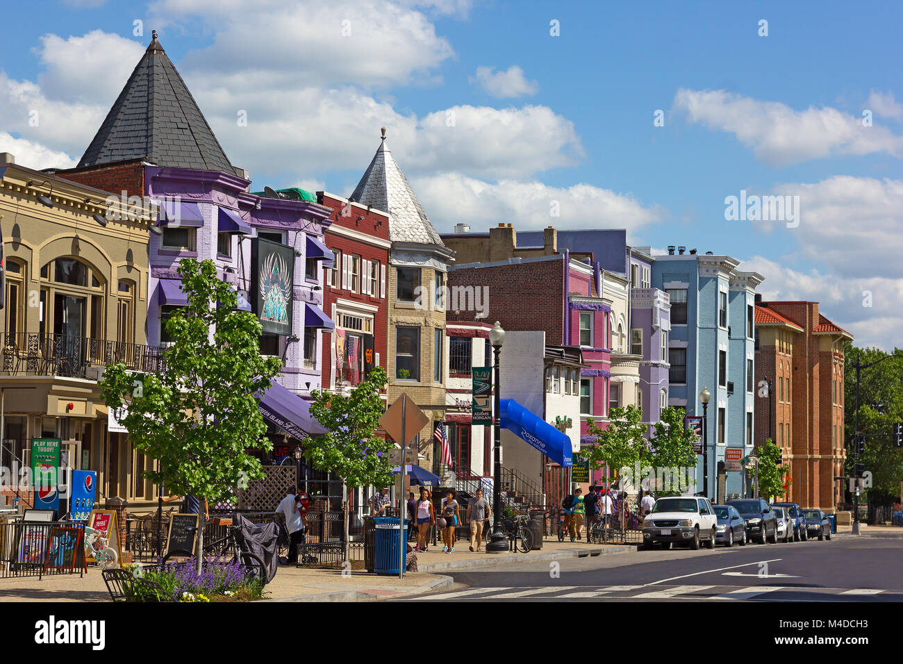 WASHINGTON DC, USA – MAY 9, 2015: Row houses and businesses in Adams Morgan neighborhood on a perfect spring day with young people walking on the stre Stock Photo