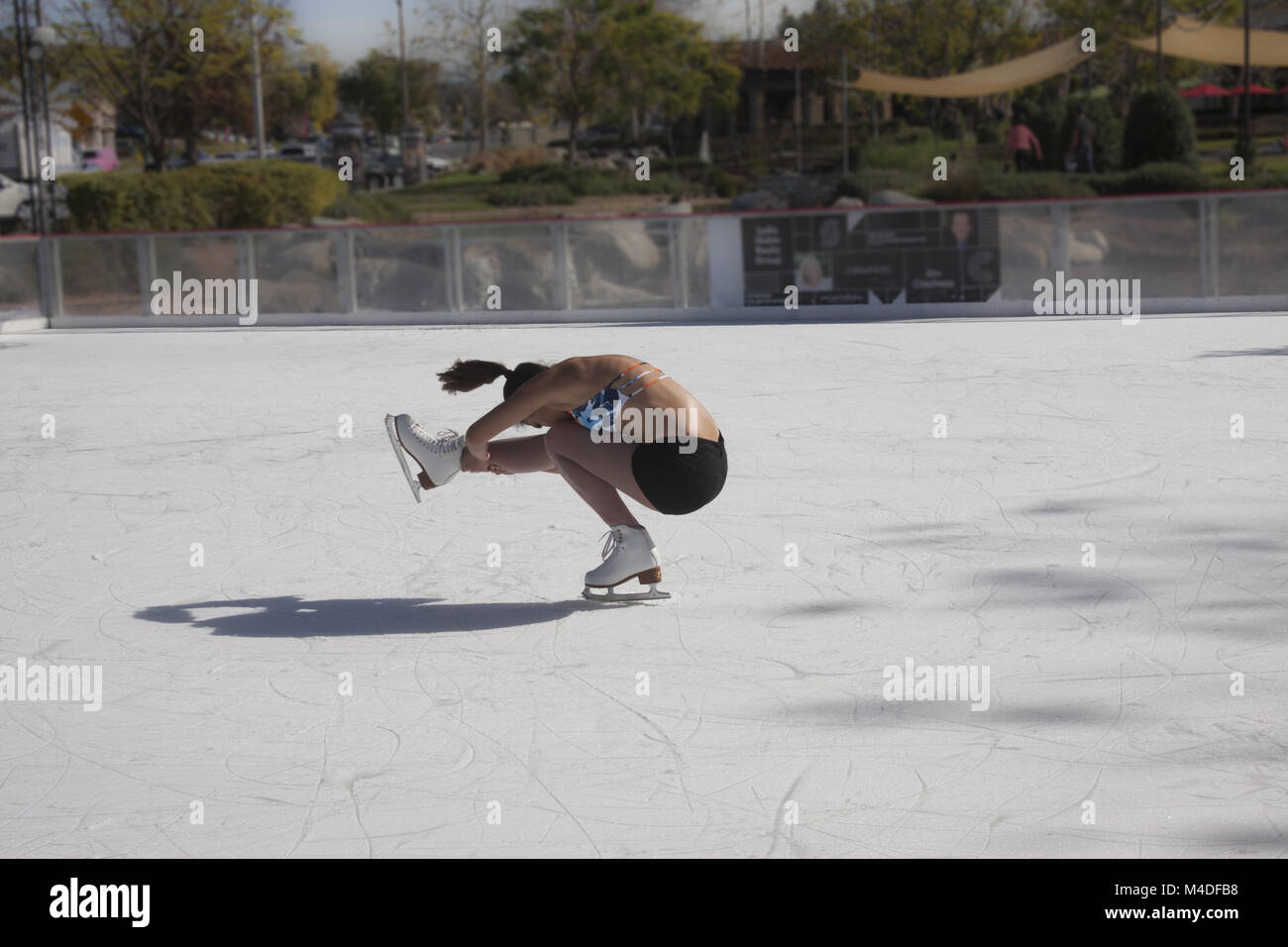 Teenage girl ice skating outdoors in shorts and a bikini top in Southern Califiornia in 85 degree winter weather Stock Photo