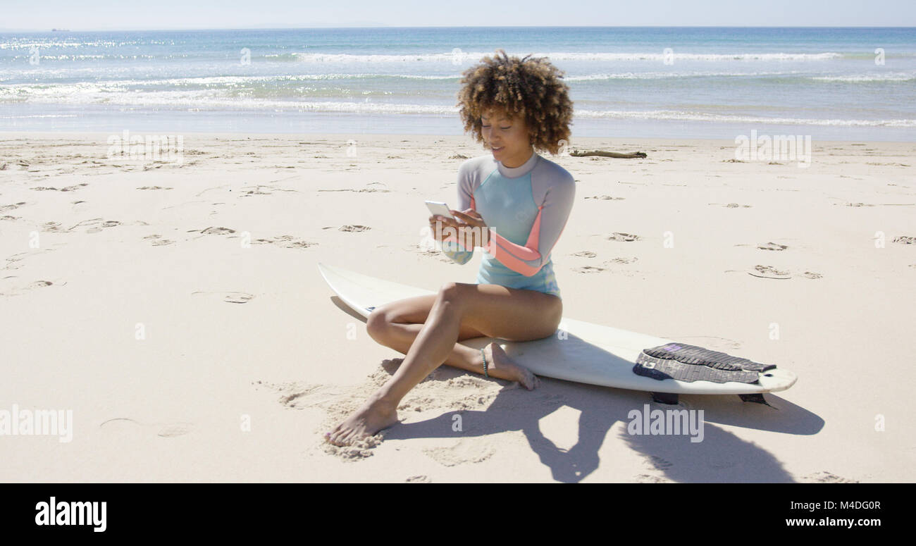 Female sitting on beach using smartphone Stock Photo