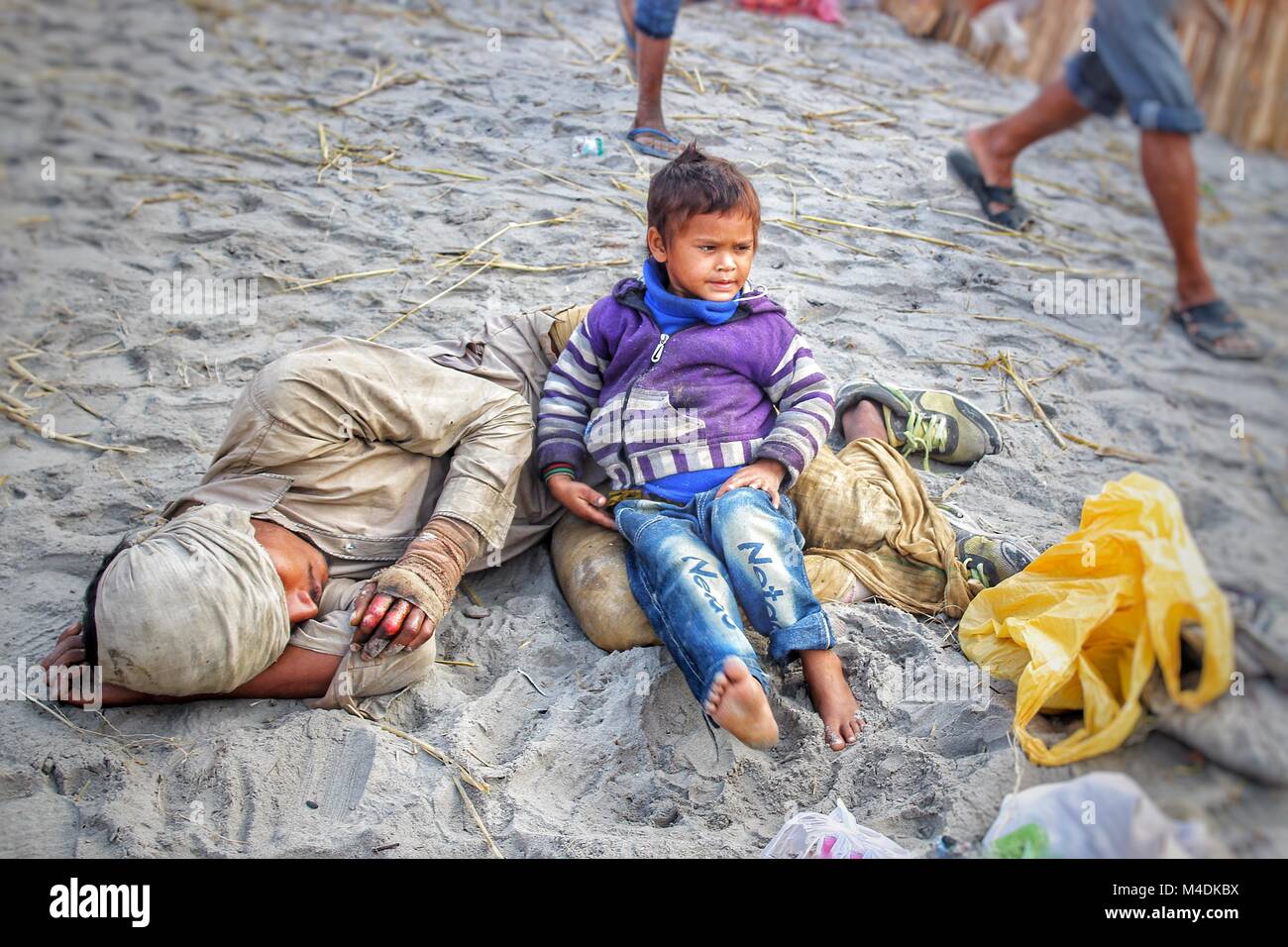 A leprous man lying on the ground beside the road at beach to begging with his little son Stock Photo