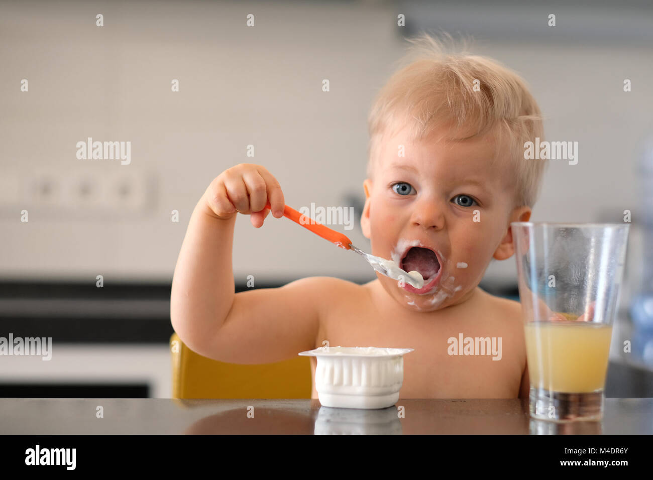 Adorable one year old baby boy eating yoghurt with spoon Stock Photo