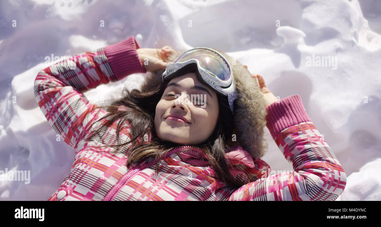 Young woman lying on snow with ski goggles Stock Photo