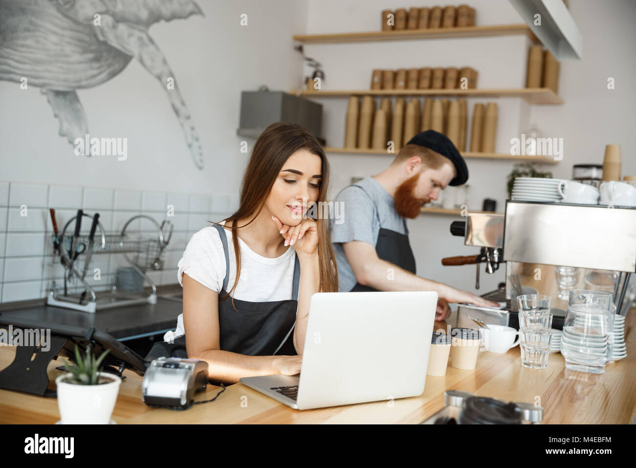 Coffee Business Concept - beautiful caucasian bartender barista or manager working and planing in laptop at modern coffee shop. Stock Photo