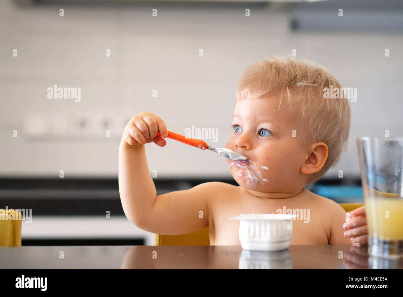 Adorable one year old baby boy eating yoghurt with spoon Stock Photo