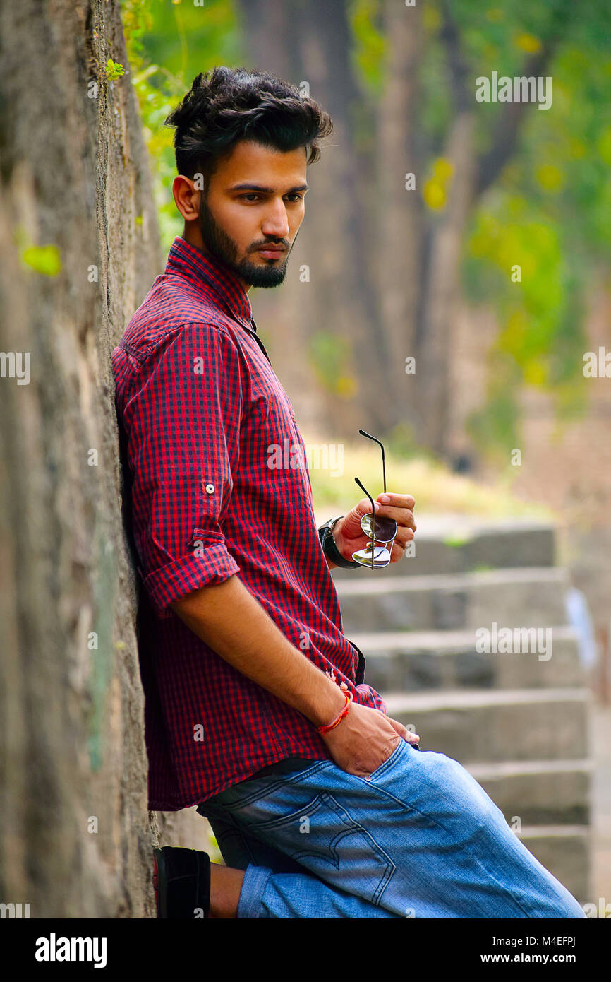 Young man with checked shirt with sun glasses in hand resting on a tree trunk, Pune, Maharashtra. Stock Photo