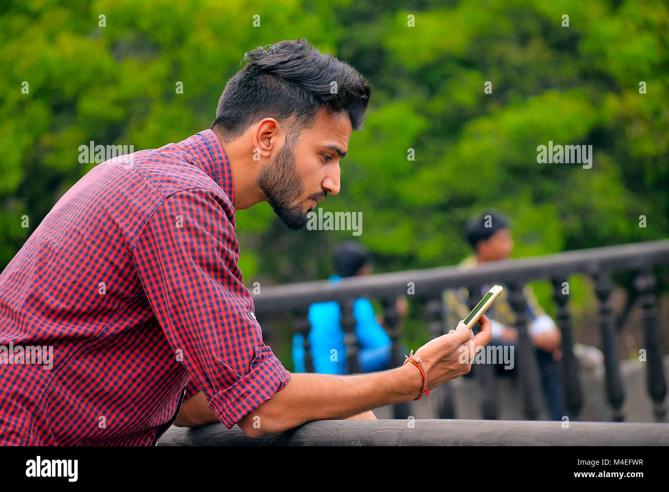Young man with checked shirt looking at cell phone, Pune, Maharashtra. Stock Photo