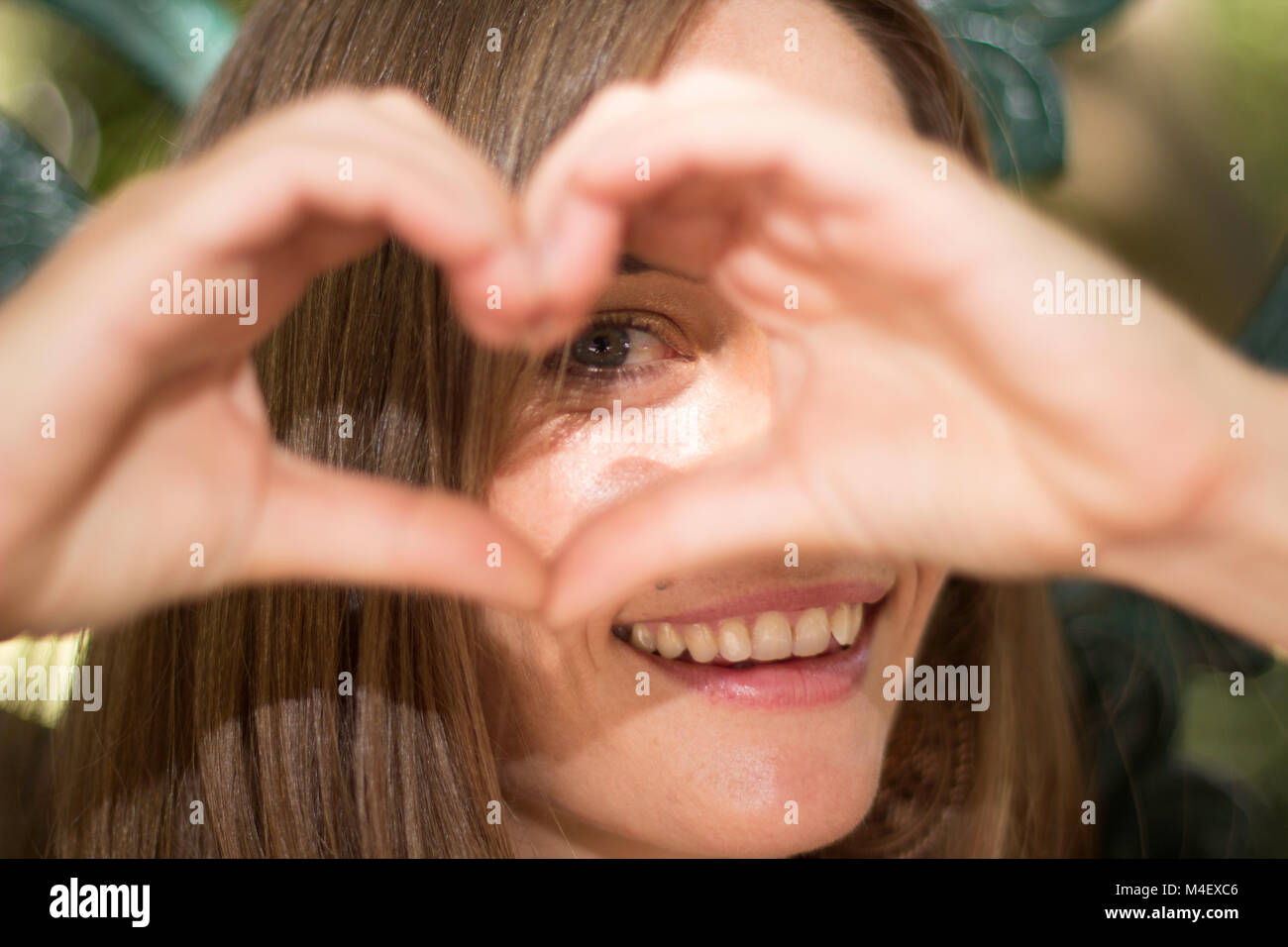 Female playing a game of peak a boo through a heart shape made with her hands Stock Photo
