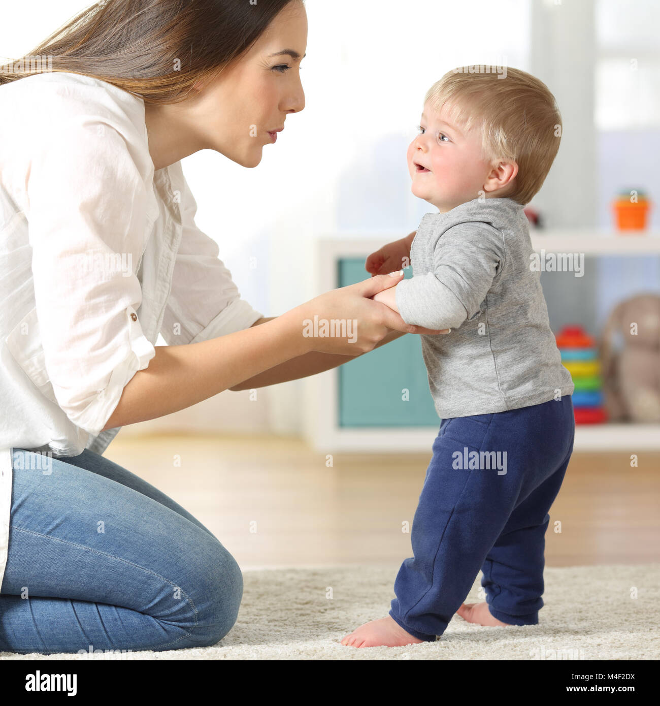 Side view portrait of a mother helping his son to walk on the floor at home Stock Photo