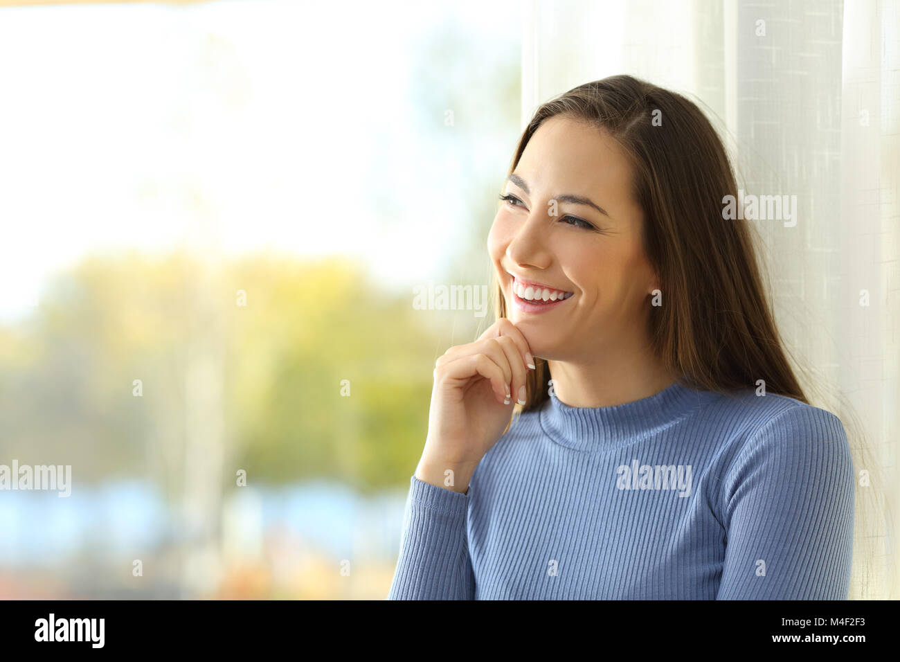 Portrait of a smiley woman thinking and looking at side  near a window at home Stock Photo