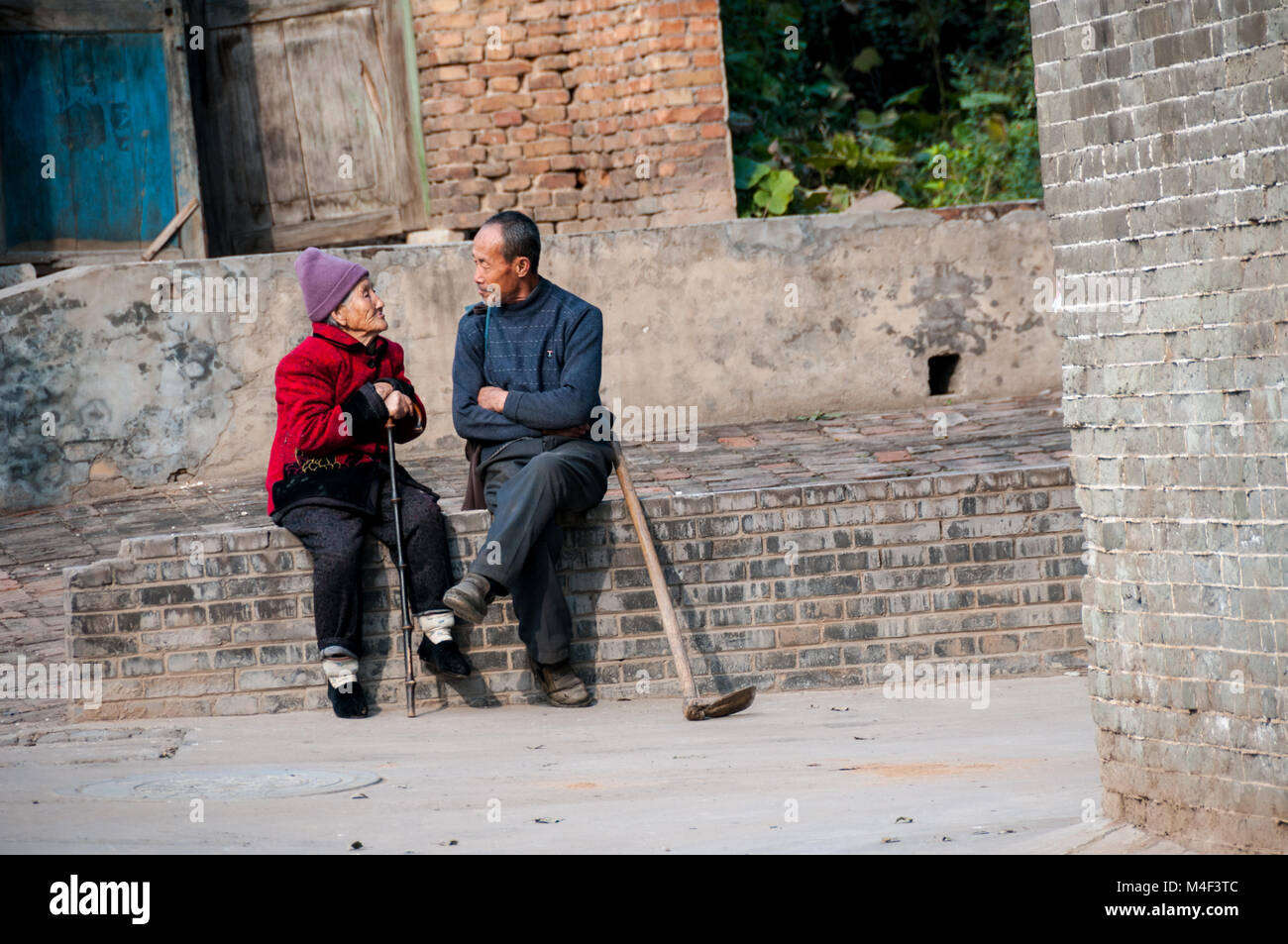 An old farmer sitting on a wall talking to an elderly lady in the Ming Dynasty village of Dangjiacun near Hancheng, Shaanxi Province, China. Stock Photo