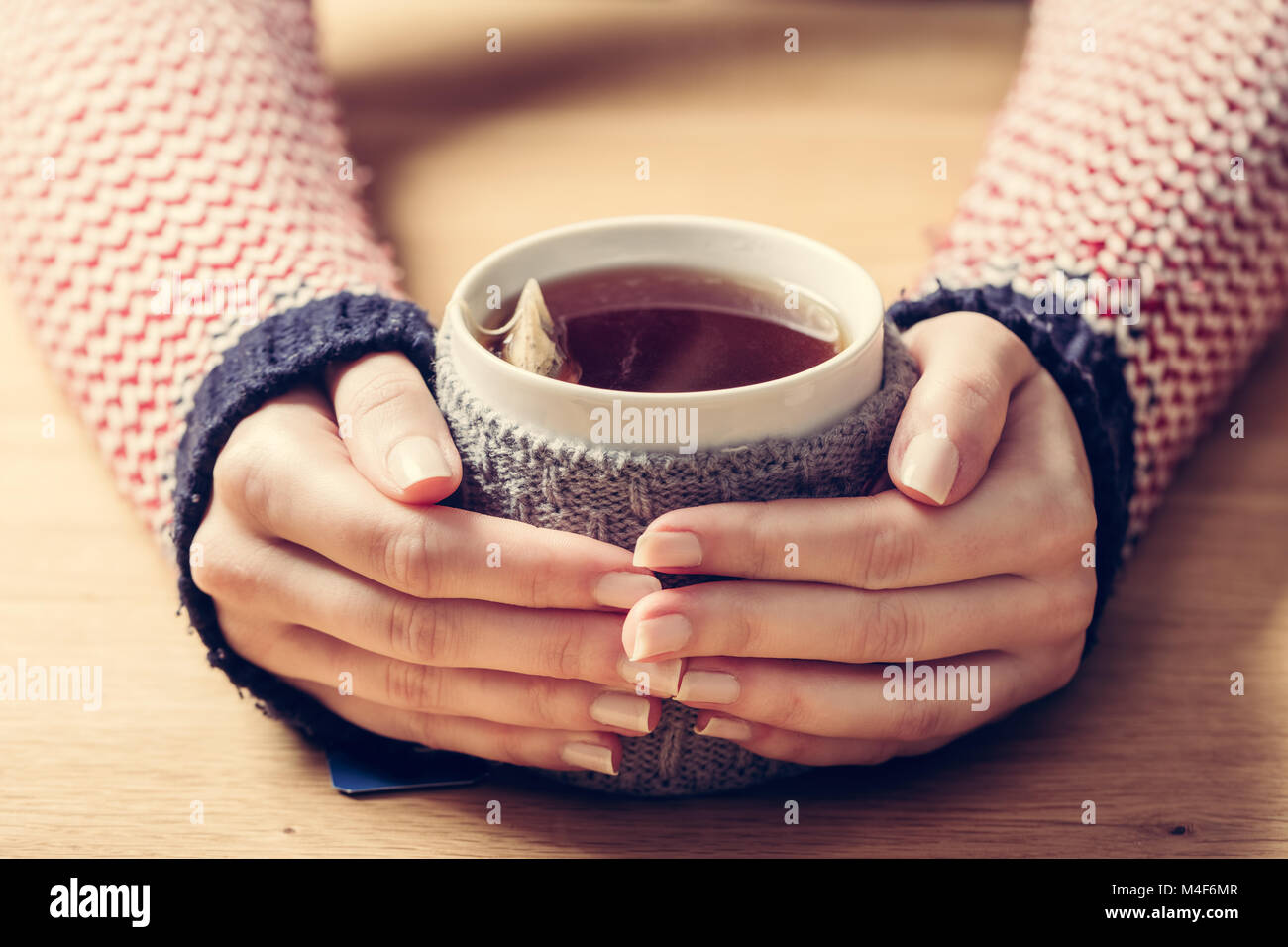 Hot mug of tea warming woman's hands in retro jumper. Stock Photo