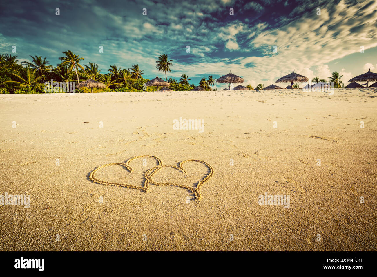 Two hearts drawn on sand of a tropical beach. Vintage Stock Photo