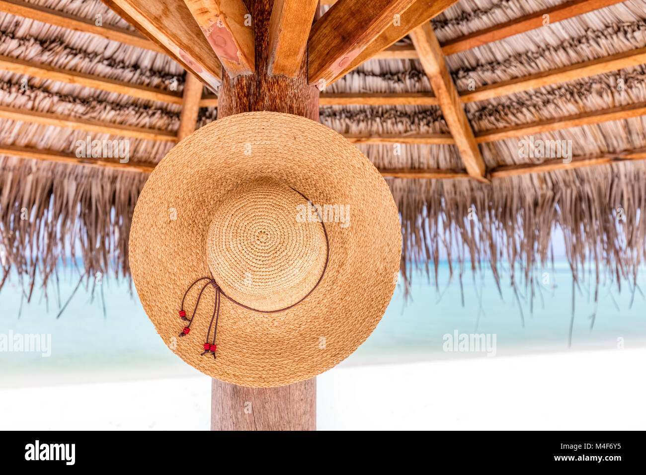 Sun hat hanging on sunshade umbrella on tropical beach. Maldives. Stock Photo