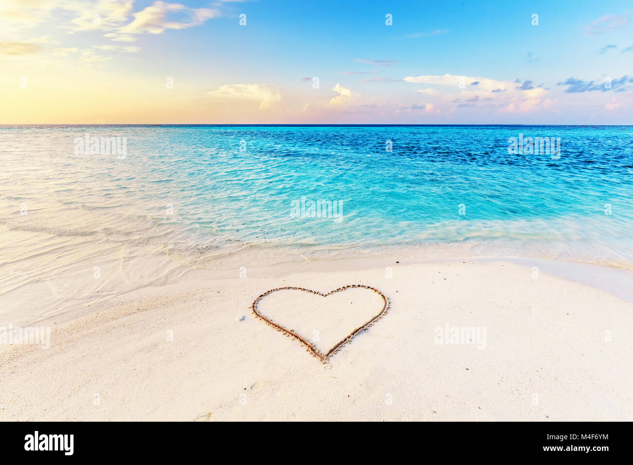 Heart drawn on sand of a tropical beach at sunset. Stock Photo