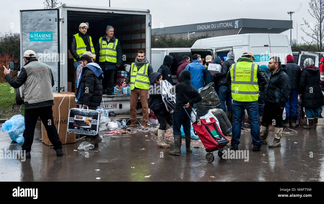 Grande-Synthe, Northern France. 31 January 2016. A delivery of aid by Belgian aid agency, Hasane is delivered and distributed to the Grande-Synthe refugee camp close to the port of Dunkirk in Northern France. In the camp conditions are grim in part due to thick mud and a lack of basic amenities. Families live in rain soaked tents and huddle around small fires for basic heat. Stock Photo