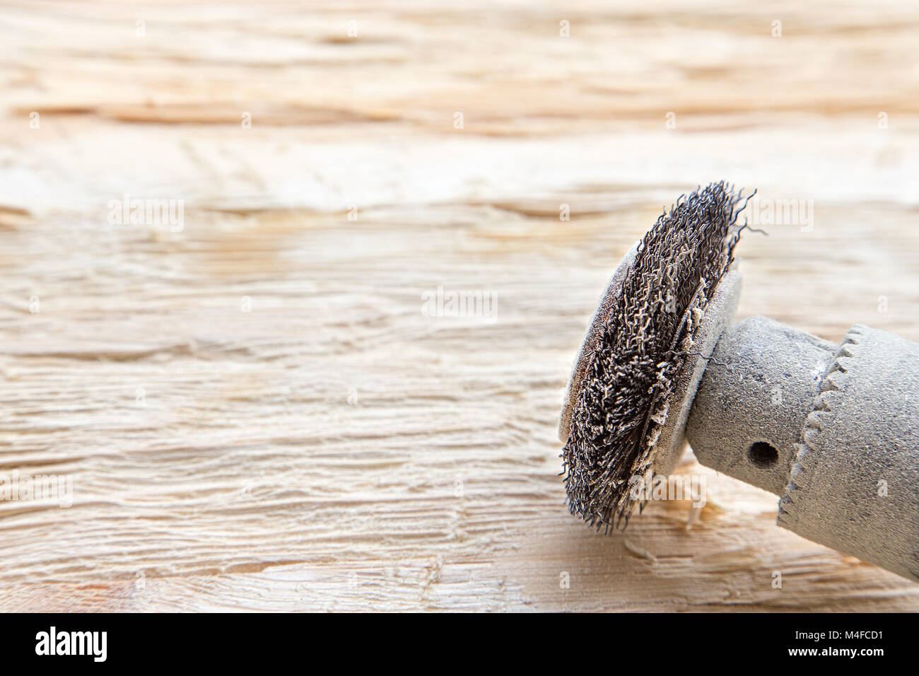 attachment on a drill, scrape, metal rotating brush. attachment is on a rough wooden surface