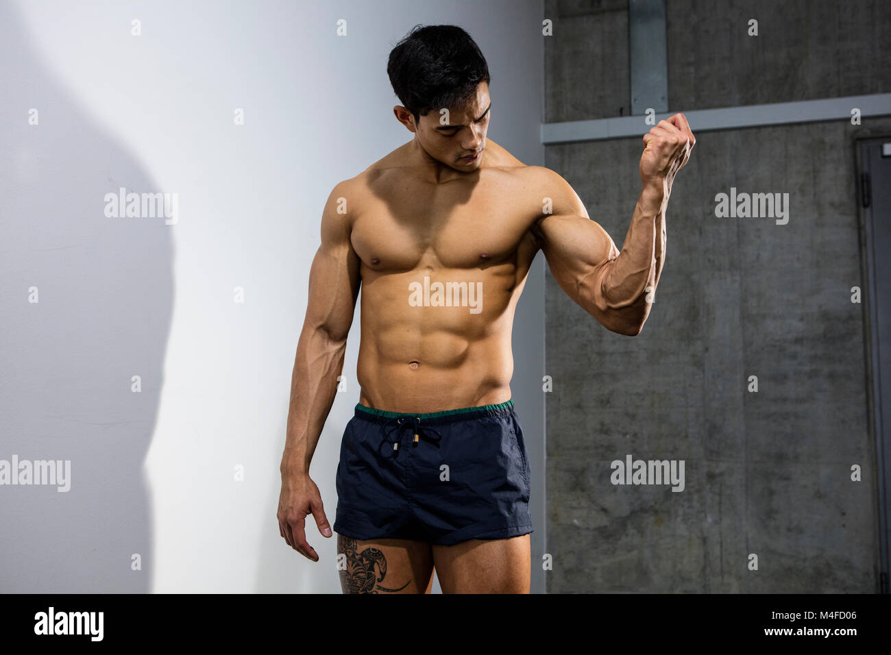 An Asian fitness model flexing his bicep muscle and looking at it Stock