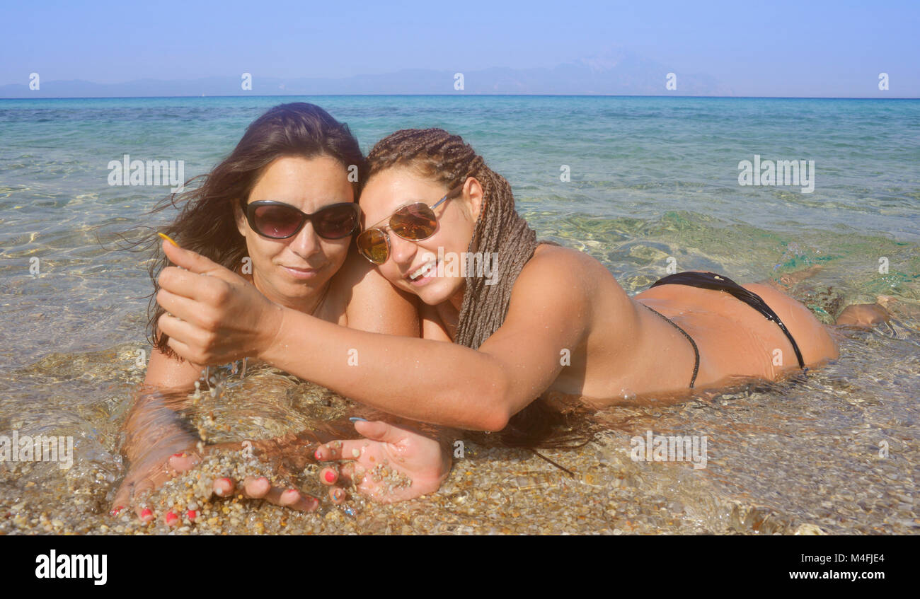 Two beautiful girls on a distant sea shore lying in the water playing with sand. Stock Photo