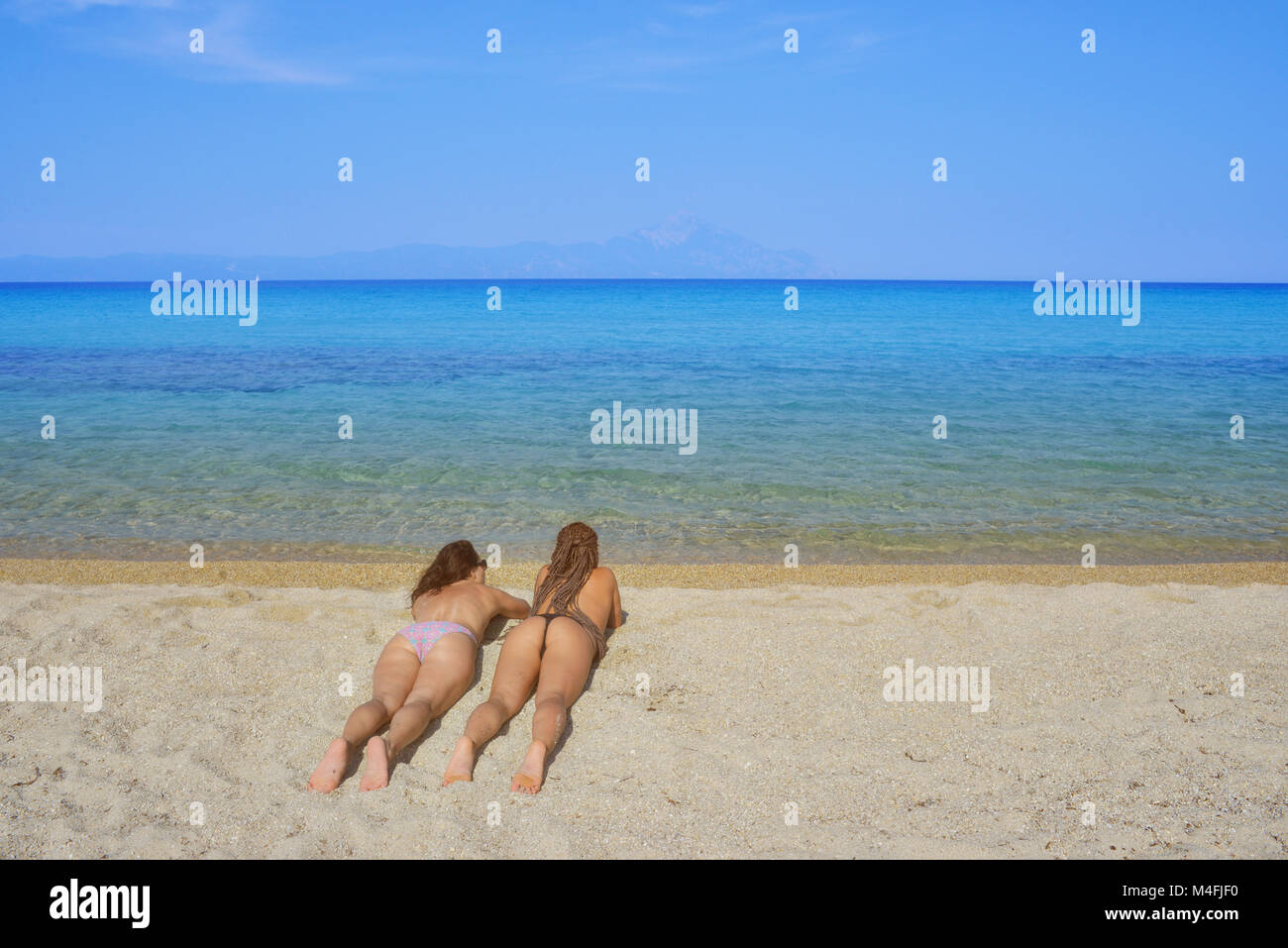 Two beautiful females in bikini lying on a sandy beach over a calm sea. Stock Photo