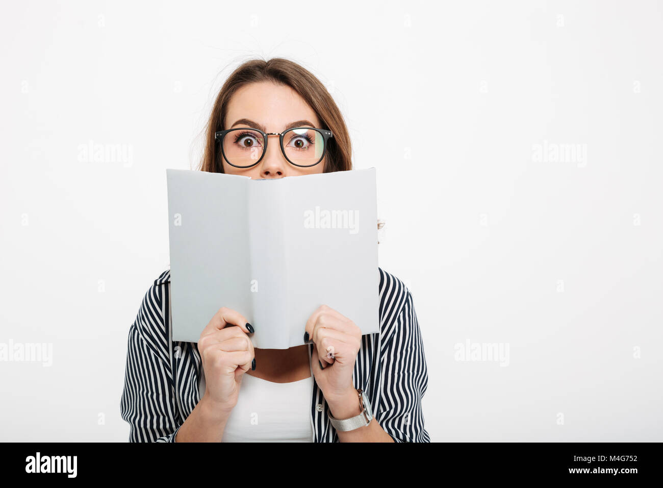 Portrait of a pretty casual girl holding opened book at her face ...