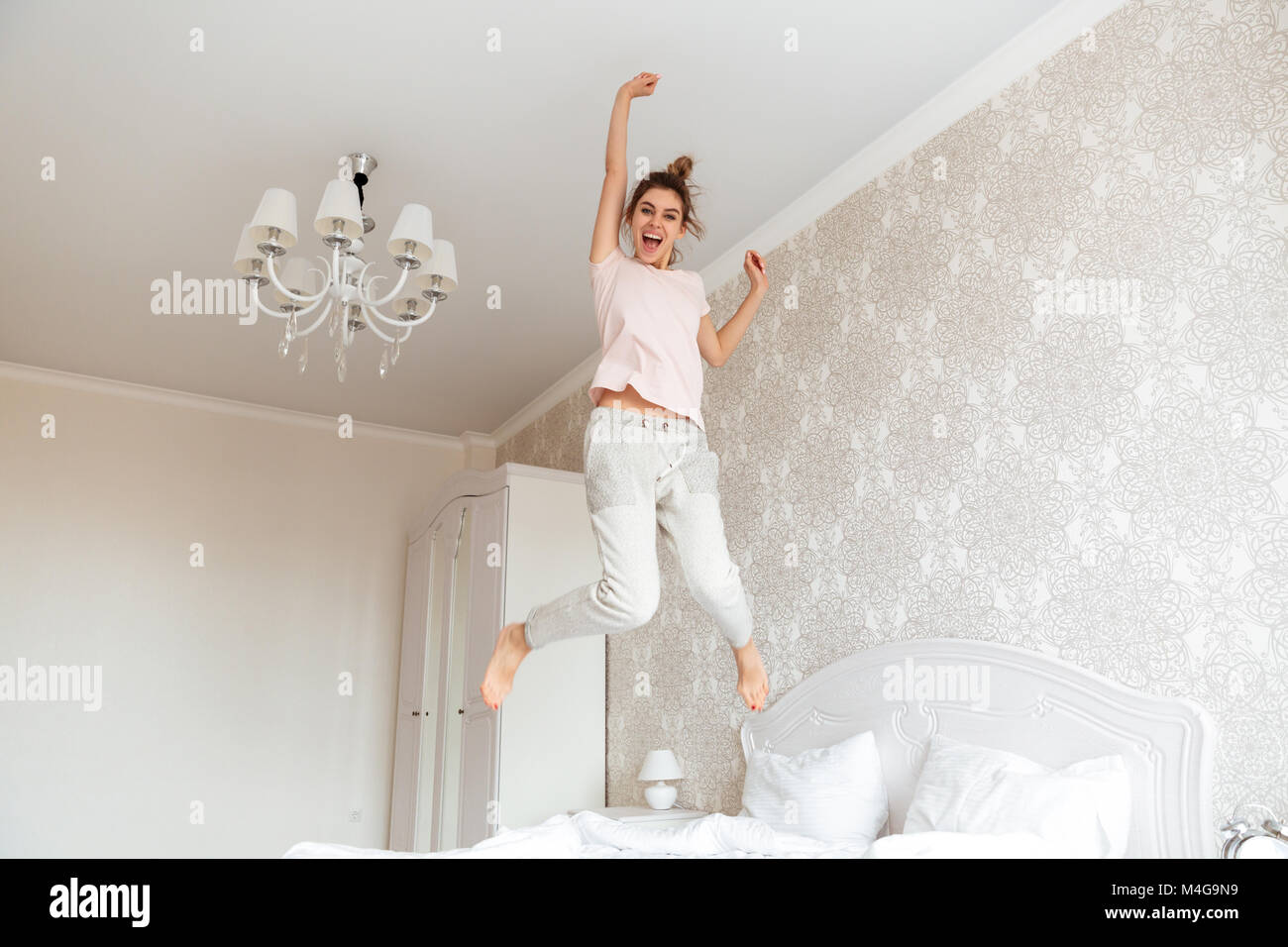 Full length image of Happy young woman having fun on bed at home Stock