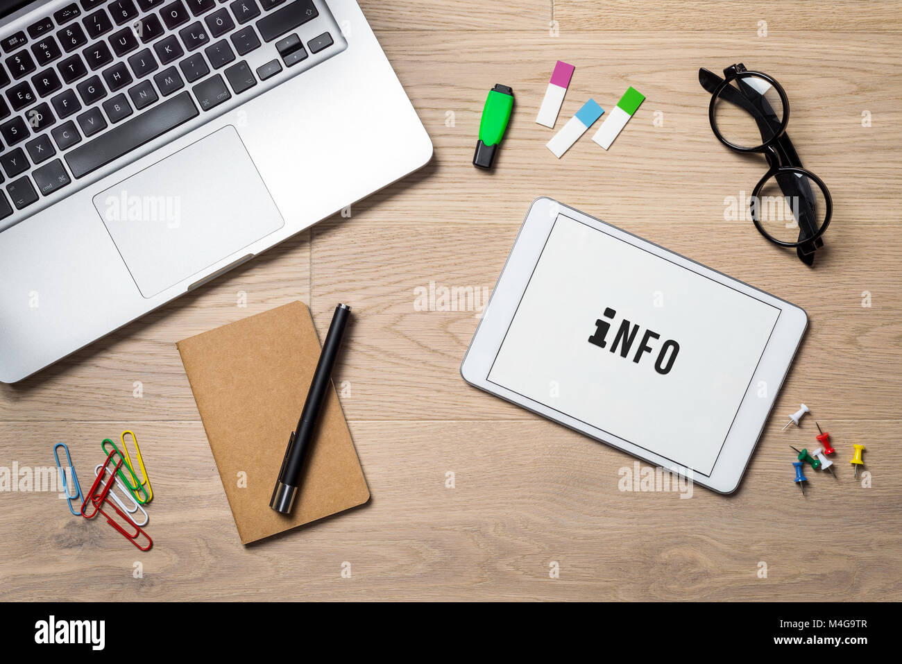 Info writing on tablet screen with laptop, notebook and glasses lying