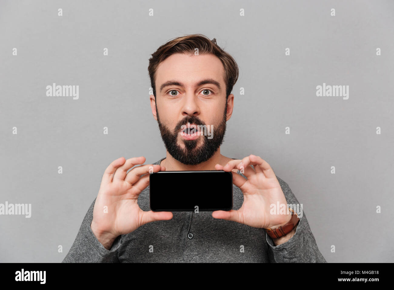 Portrait of a surprised casual man showing blank screen mobile phone ...