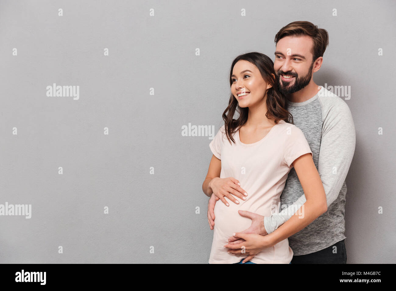 Portrait of a smiling young man hugging his pregnant wife while ...