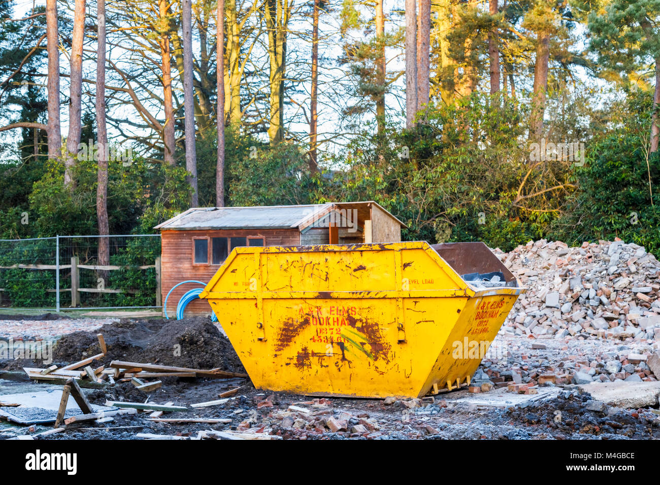 Real estate construction site: yellow skip in the remains of the demolition of a residential house property on a building site prior to redevelopment Stock Photo