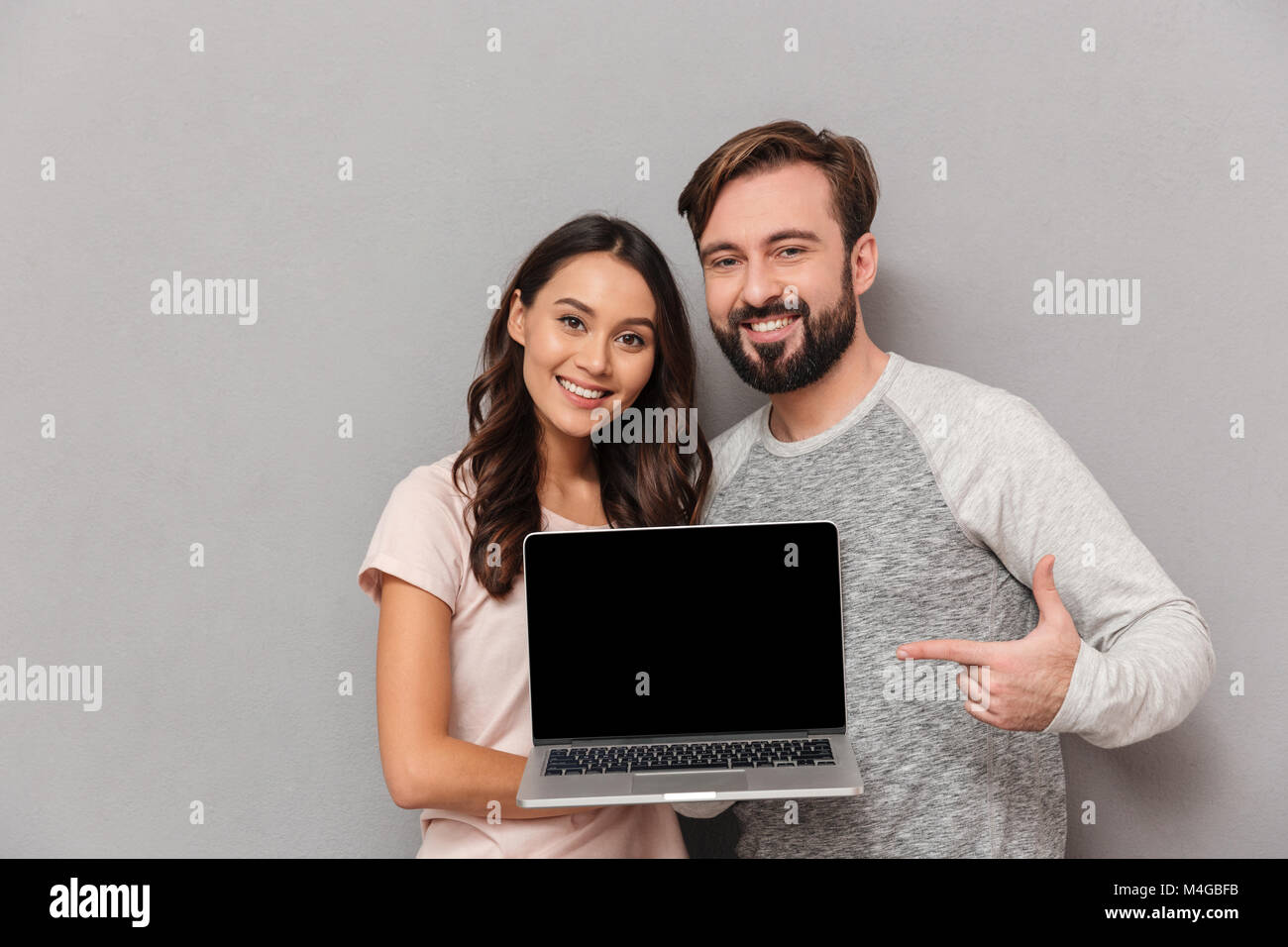 Portrait of a smiling young couple showing blank screen laptop computer ...