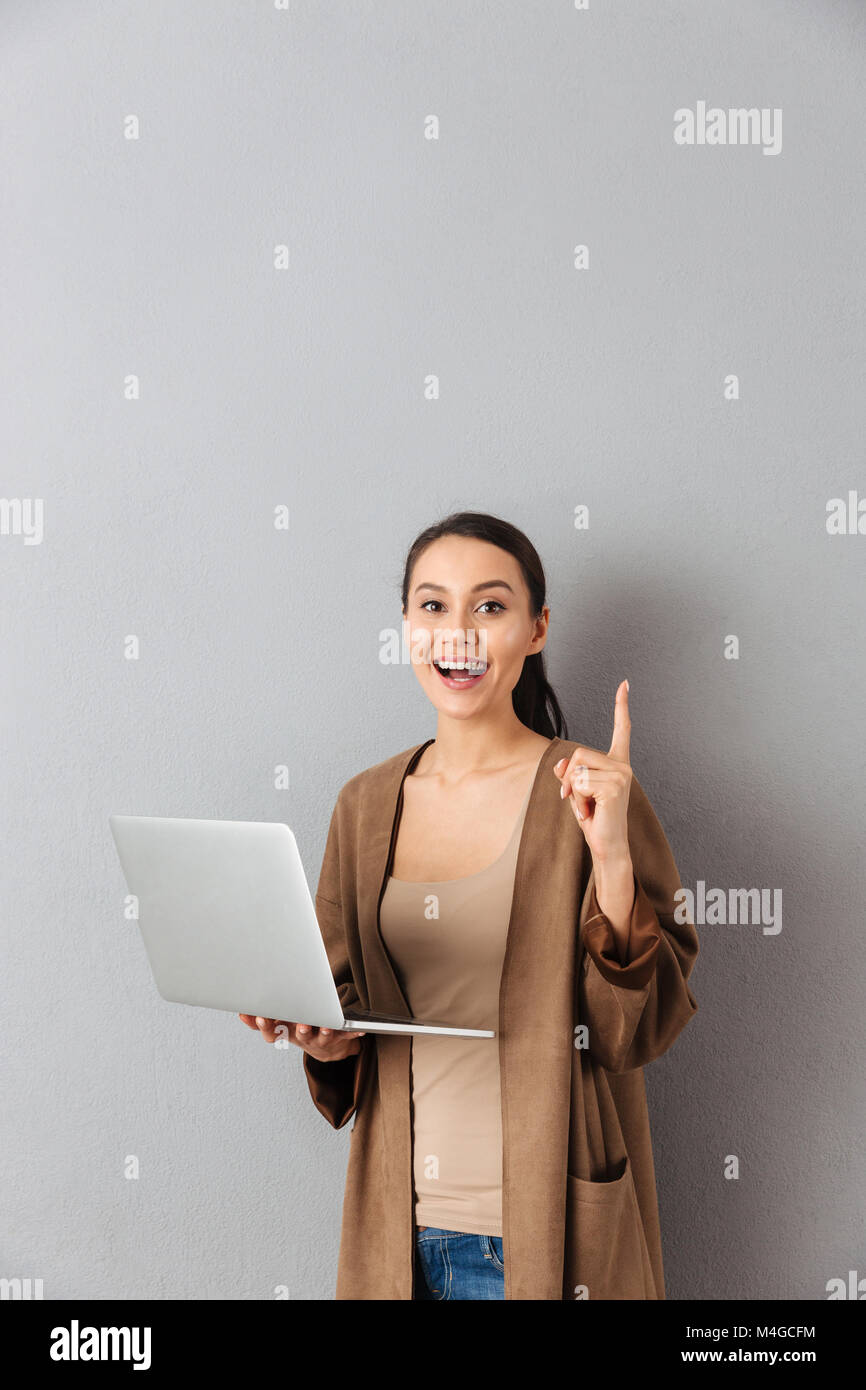 Portrait of an excited young asian woman holding laptop computer while ...
