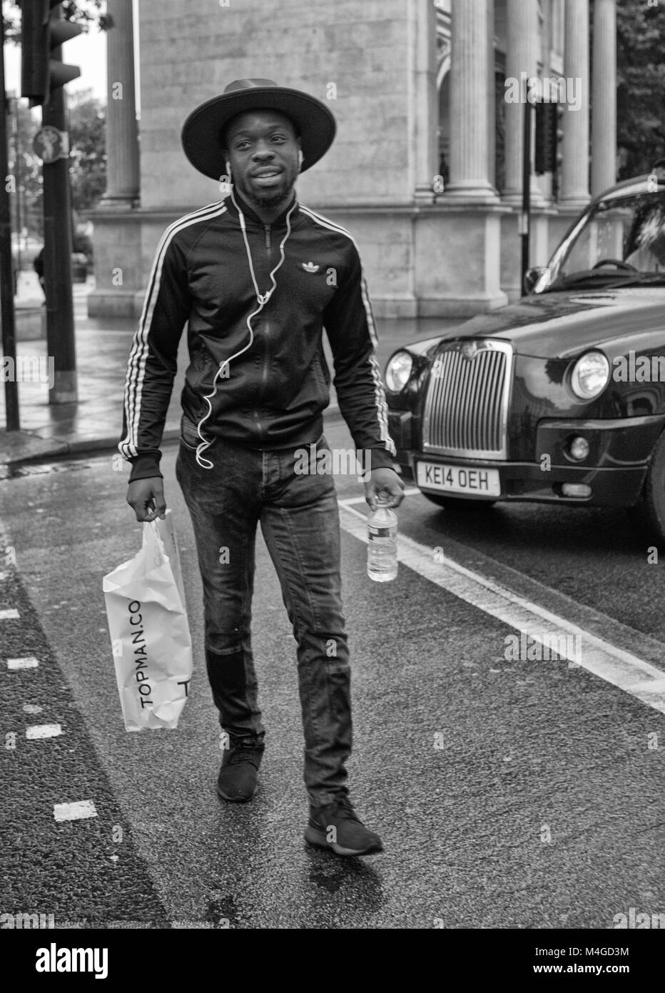Black & White Photograph of a young man walking past Marble Arch, London, England, UK. Credit: London Snapper Stock Photo