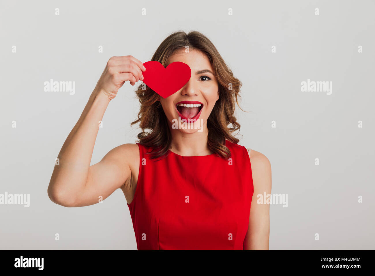 Portrait of a cheerful young woman dressed in red dress holding paper ...