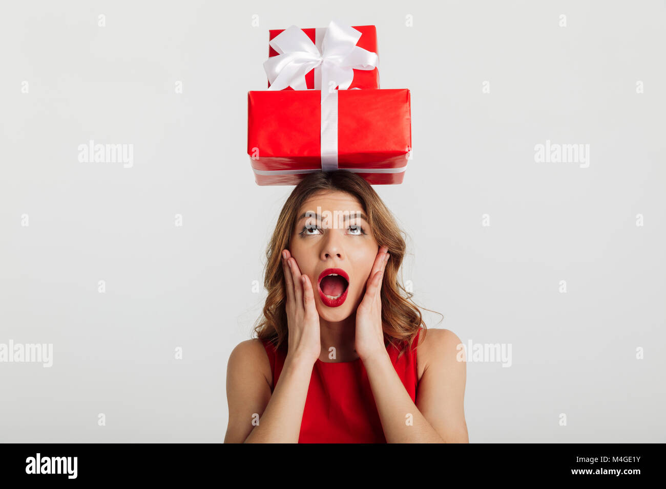 Portrait of a surprised young woman dressed in red dress holding stack ...