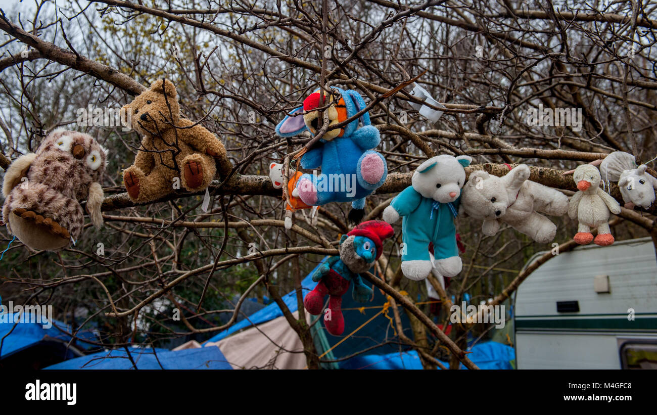 Grande-Synthe, Northern France. 31 January 2016. Children's toys hang from a tree near the entrance to the camp. Grande-Synthe refugee camp close to the port of Dunkirk in Northern France. In the camp conditions are grim in part due to thick mud and a lack of basic amenities. Families live in rain soaked tents and huddle around small fires for basic heat. Stock Photo