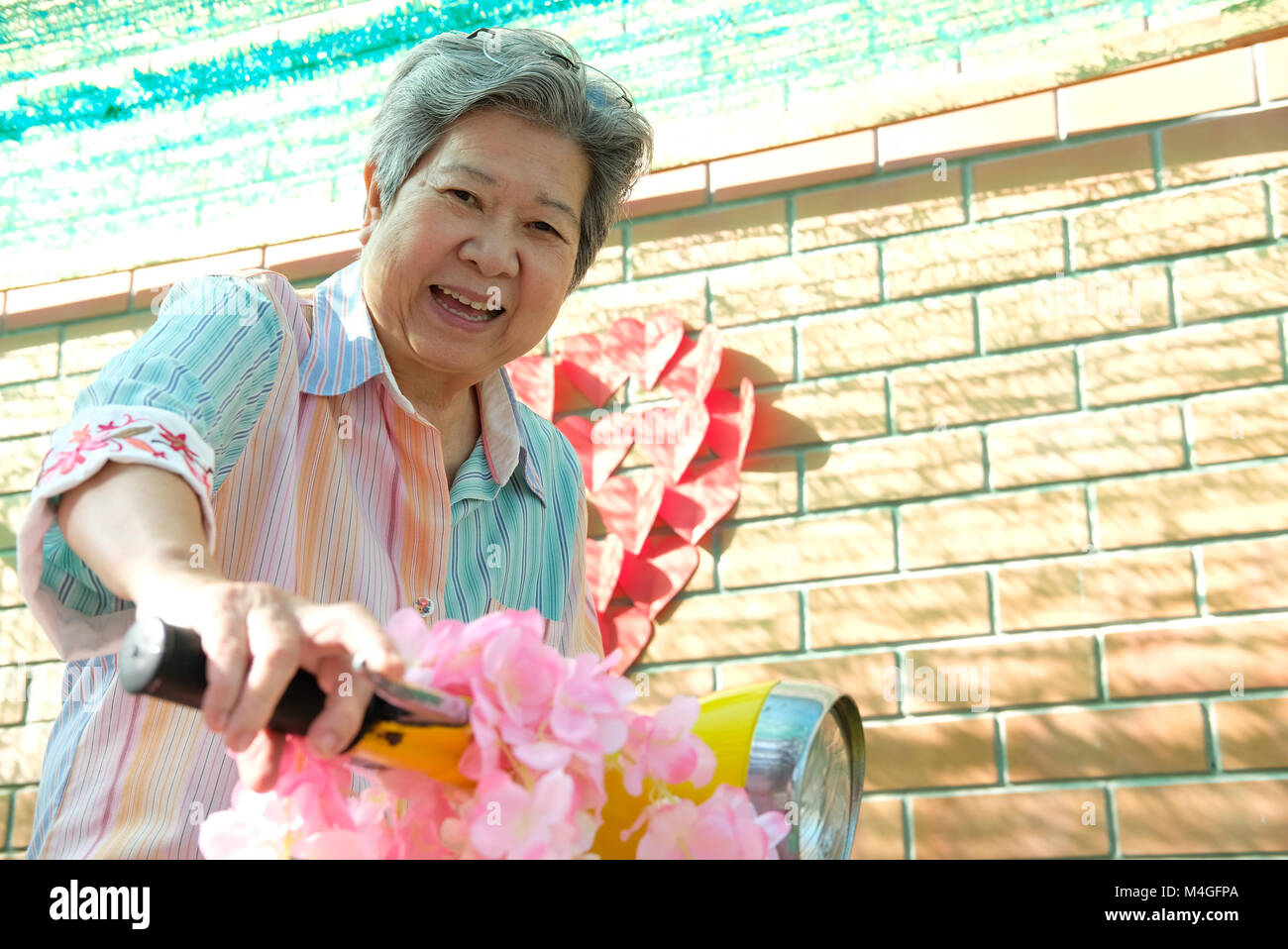 asian elder woman riding motorcycle. happy elderly female on yellow motorbike. fun mature lifestyle concept Stock Photo