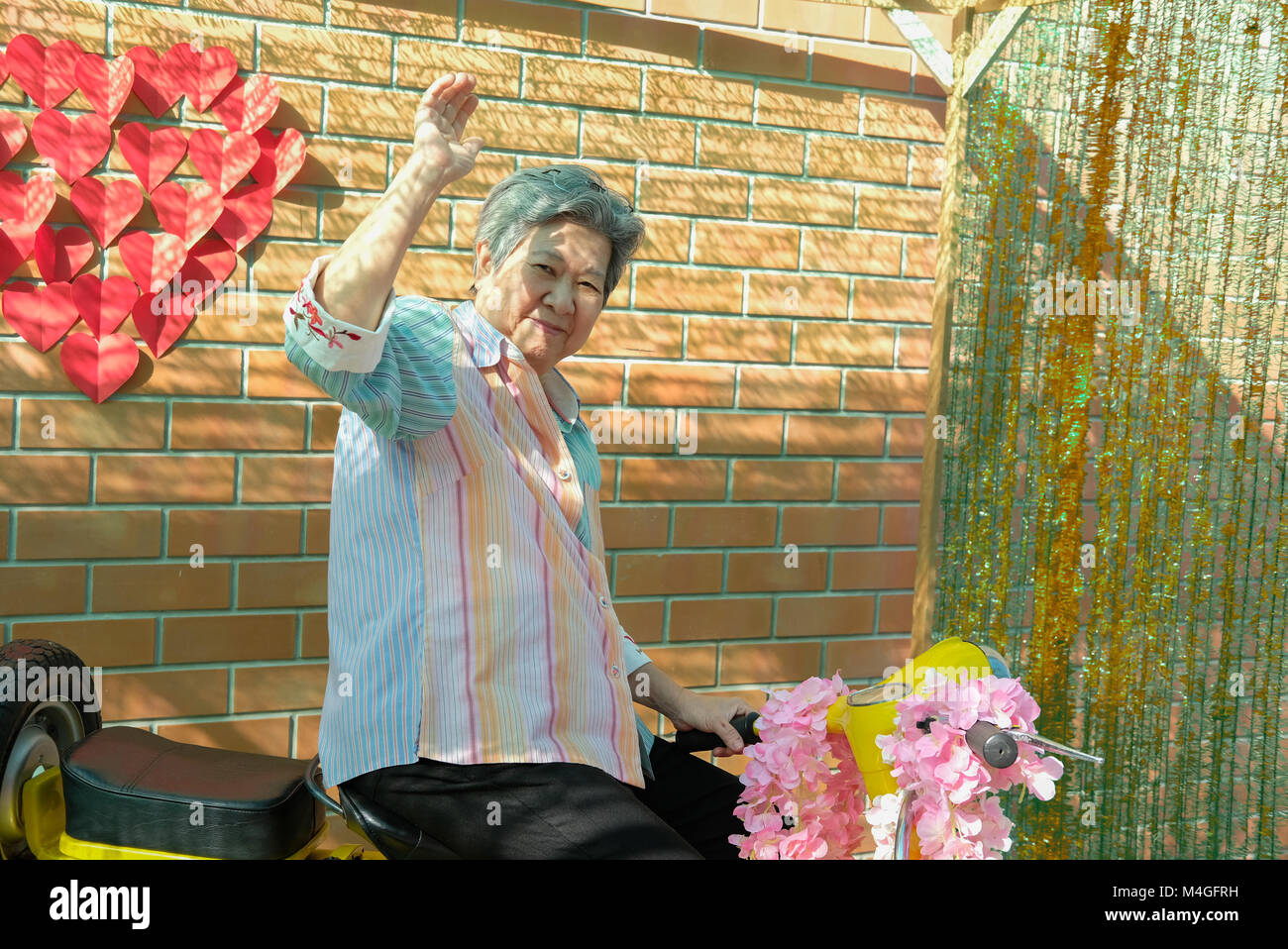 asian elder woman riding motorcycle. happy elderly female on yellow motorbike. fun mature lifestyle concept Stock Photo