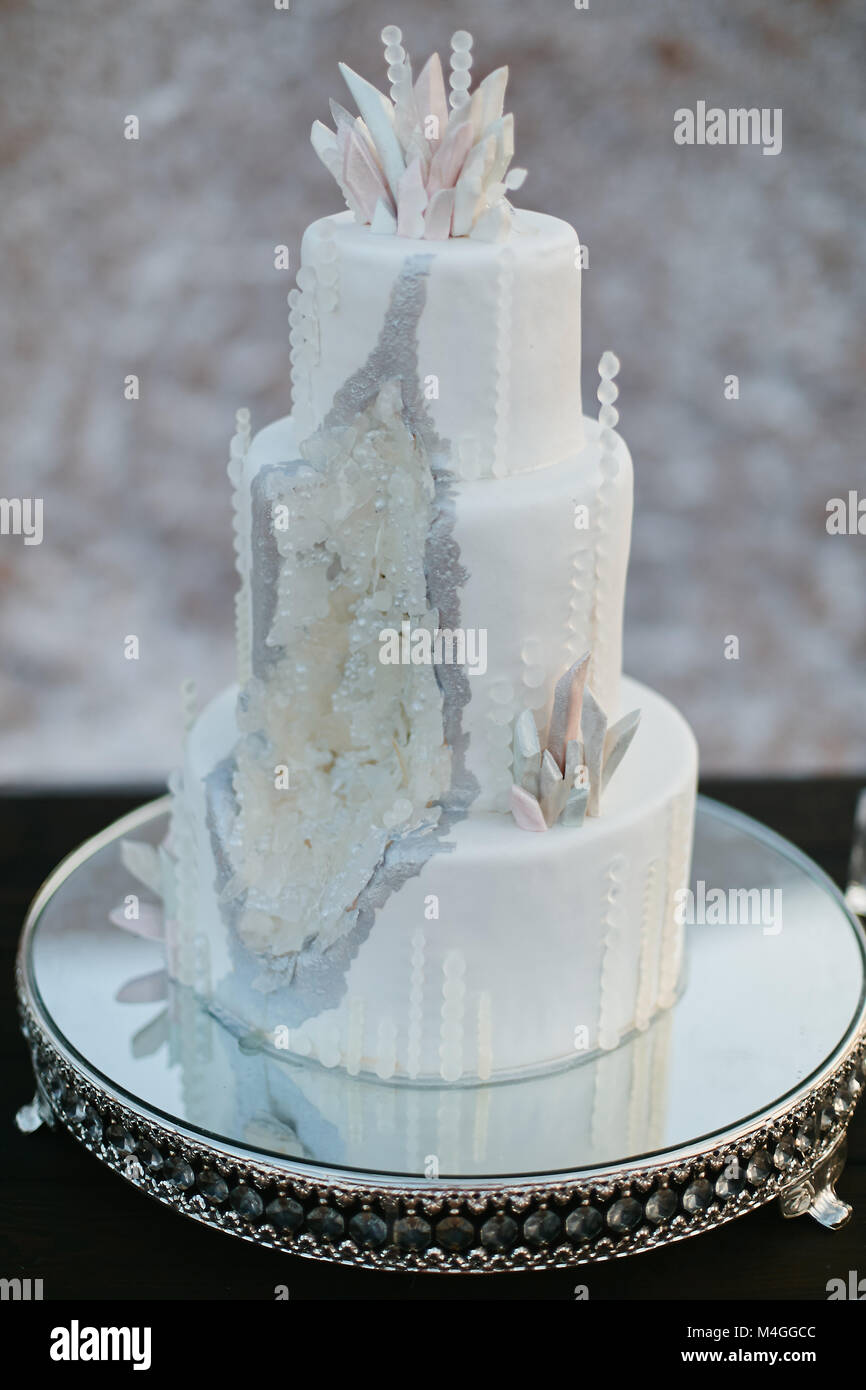 Stylish white wedding cake with crystals on a mirror stand Stock Photo