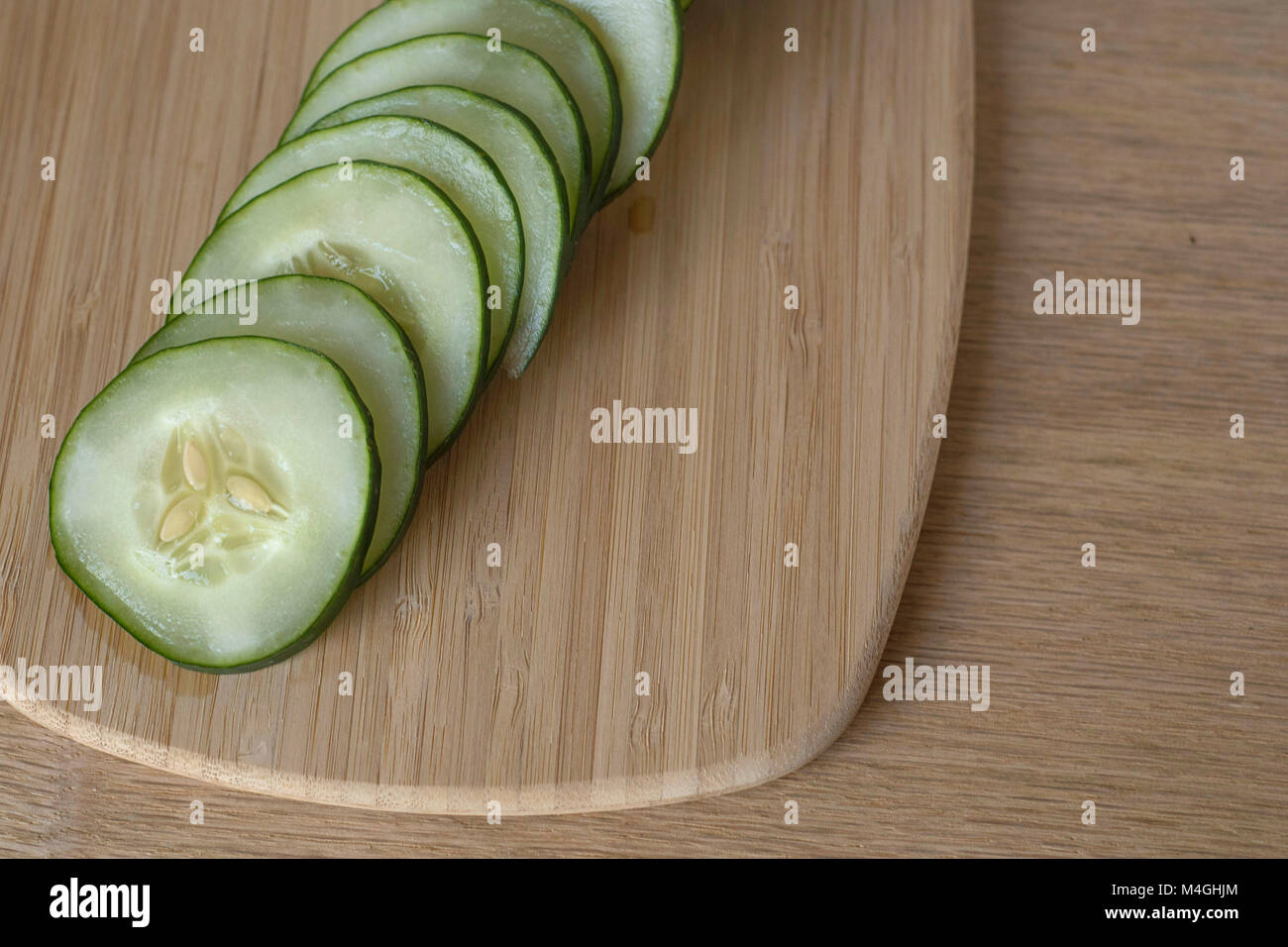 Slices of a Cucumber with Seeds Fanned Out on a Bamboo Cutting Board Overhead View Stock Photo