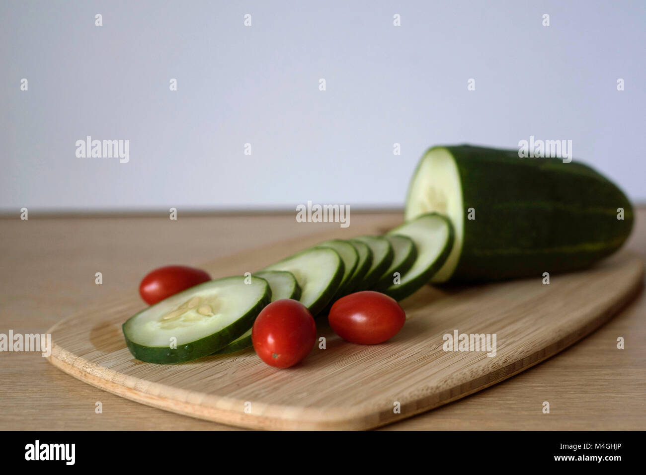 Slices of Cucumber with Red Tomatoes Ready for Meal Prep on a Cutting Board Stock Photo