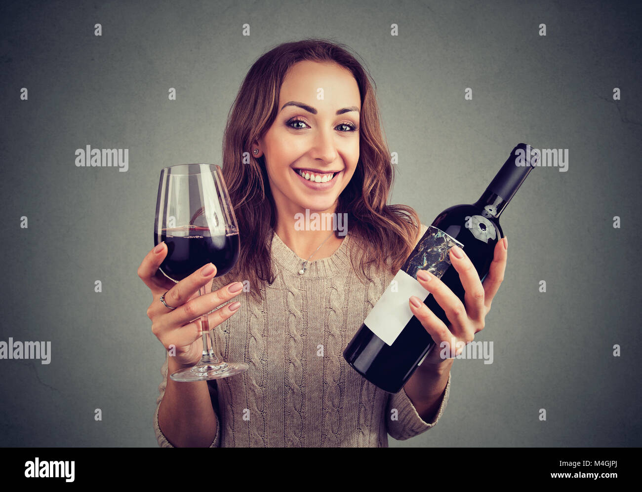 Young woman holding glass of wine and bottle looking happily at camera enjoying taste. Stock Photo