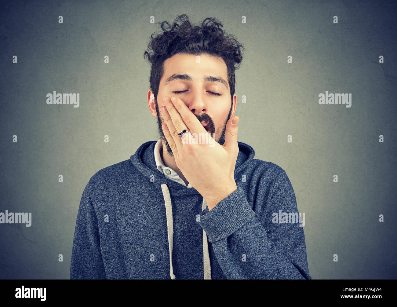 Young hipster man yawning in laziness covering mouth on gray background. Stock Photo