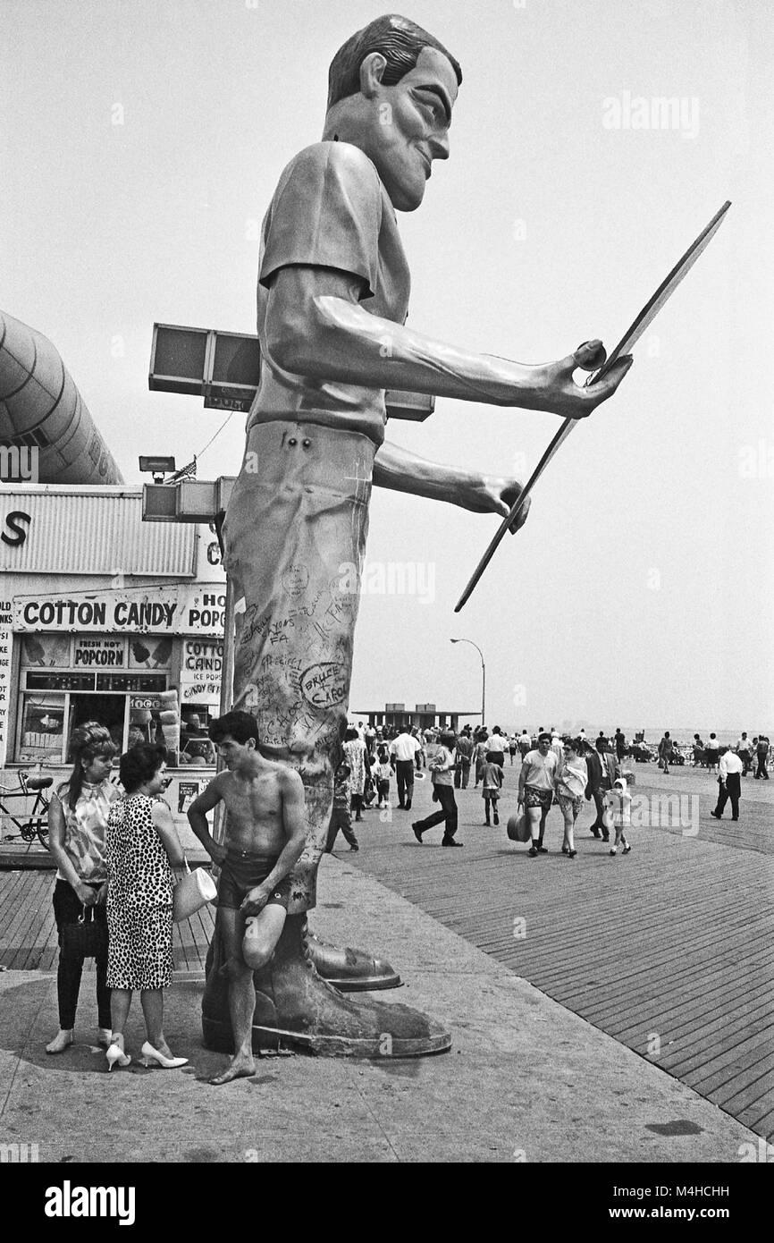People walk by a giant statue on a boardwalk on Coney Island beach in