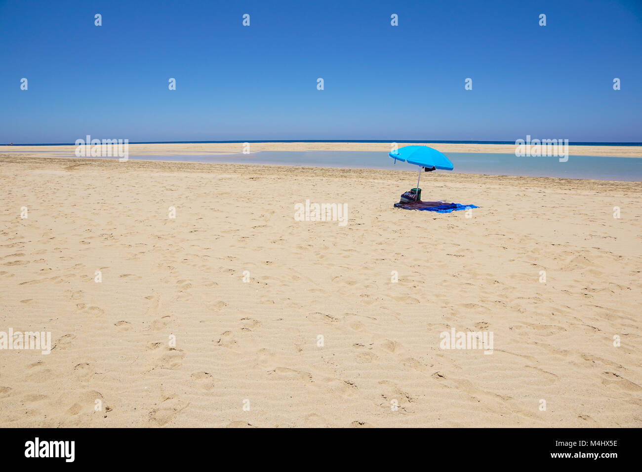 Desert beach with sun shades, tranquil sea, blue sky, clouds . Summer travel destination. Stock Photo