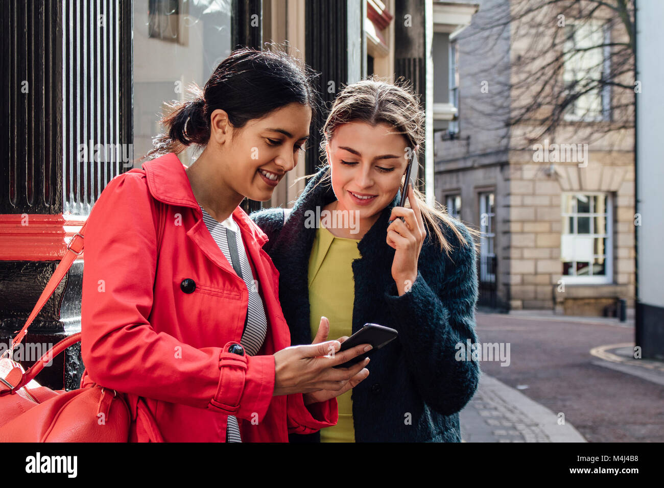 Two businesswomen are organising transport to work. One of the women is holding her smart phone which they are both looking at. The other girl is talk Stock Photo