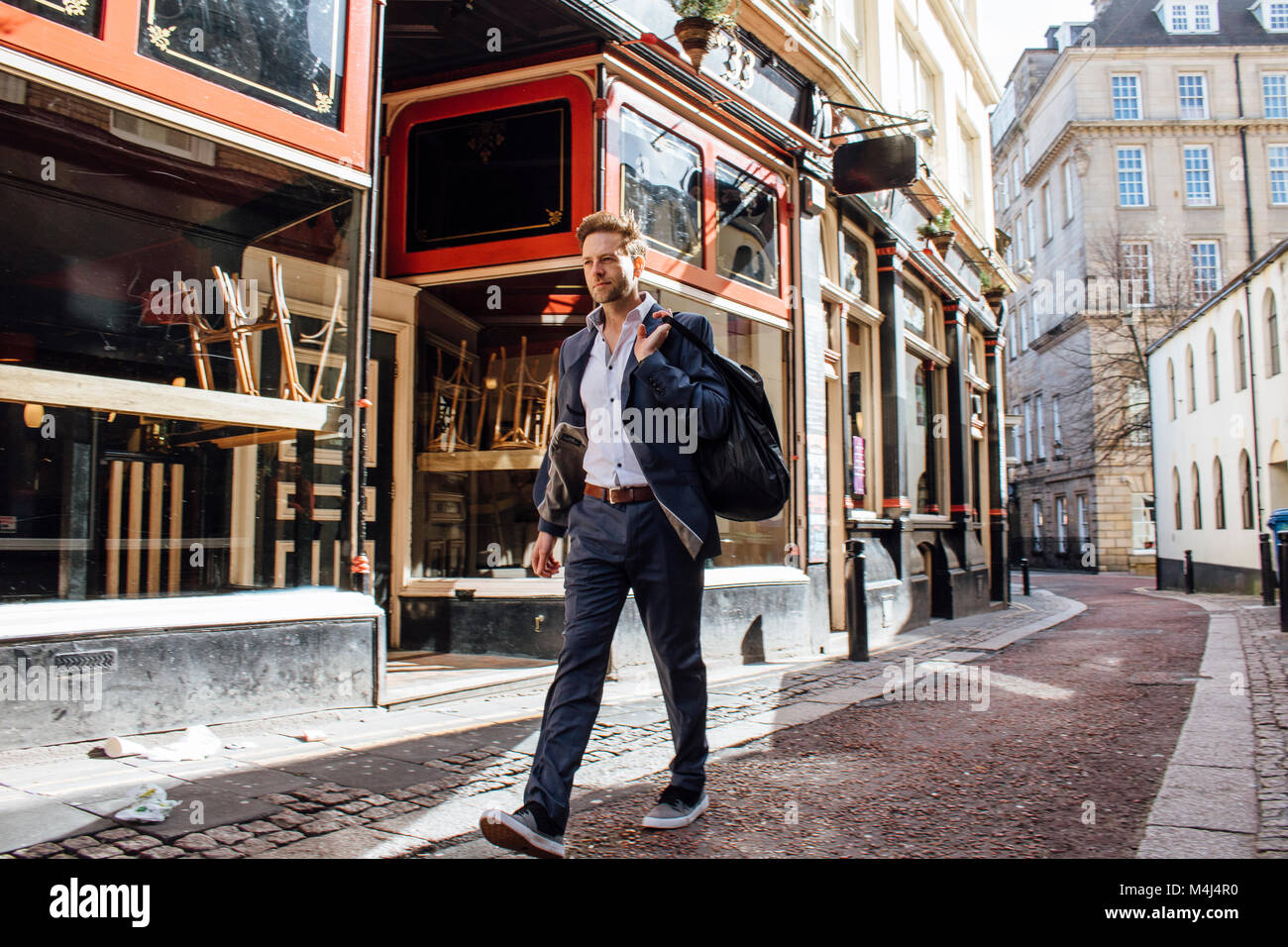 Businessman is walking to work in the city. He is wearing trainers and carrying a gym bag over his shoulder. Stock Photo